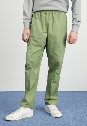Person wearing light green cargo pants, white sneakers, and a gray sweatshirt standing on blue carpeted floor.