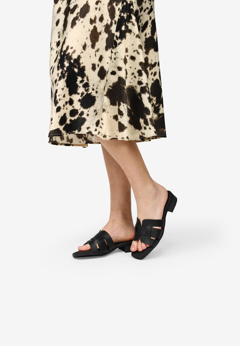 Sandalias de cuero negro de tipo slide con tacón cuadrado, que cuentan con un diseño de punta abierta y correas trenzadas. La textura es suave y flexible.