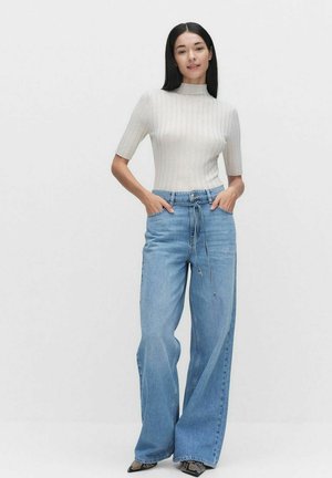 Ljust grå, ribbad kortärmad topp i kombination med högmidjade, löst sittande blå denimjeans. Texturerad tyg med en avslappnad passform och framhävd midja.