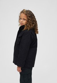 Veste cargo noire avec un col, des poches avant et une coupe décontractée. Le tissu a une texture lisse. Portée par un enfant avec des cheveux bouclés.