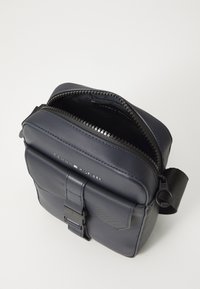 Dark blue crossbody bag made from durable material, featuring a zip closure, adjustable strap, and front flap with hardware detail.