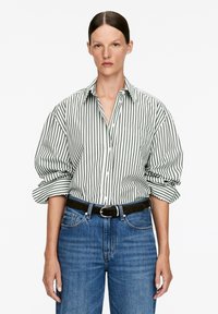 White shirt with green vertical stripes, button-up design, and rolled sleeves. Paired with blue denim jeans and a black belt.