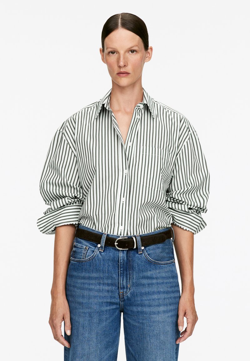 White shirt with green vertical stripes, button-up design, and rolled sleeves. Paired with blue denim jeans and a black belt.