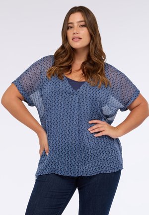 Blaue Bluse mit Muster, lockerer Passform, V-Ausschnitt und kurzen Ärmeln. Hergestellt aus leichtem, halbtransparentem Stoff mit runden Motiven.