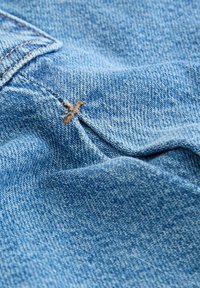 Tissu en denim de couleur bleu clair avec un motif de tissage visible. Une seule couture marron est présente sur la couture.