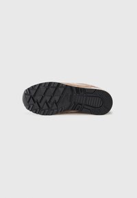 Braune Wildleder-Sneaker mit einer strukturierten schwarzen Gummisohle, die ein Zickzackmuster aufweist. Das Design umfasst verstärkte Bereiche für zusätzlichen Halt.
