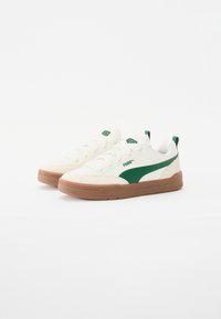 Hvite sneakers med grønne detaljer og en brun gummisåle. Har en glatt tekstur, avrundet form og klassisk snøring.