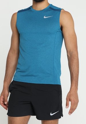 Homme portant un débardeur de sport bleu et un short Nike noir sur un fond clair uni.