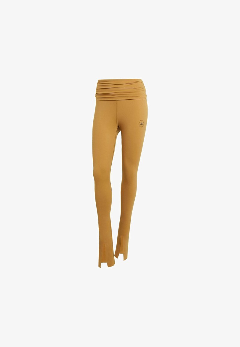 Mustard-colored leggings with a ruched waistband, flared hem, and logo detail on the side, made from stretchy, smooth fabric.