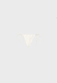 Bas de bikini blanc avec liens latéraux réglables sur un fond gris clair uni.