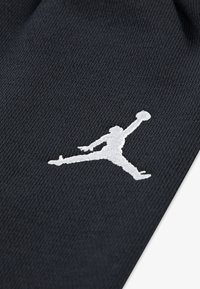 Sort stofsok med et broderet hvidt Jumpman-logo. Teksturen er glat med et strikket mønster og ingen synlige hardware eller detaljer.