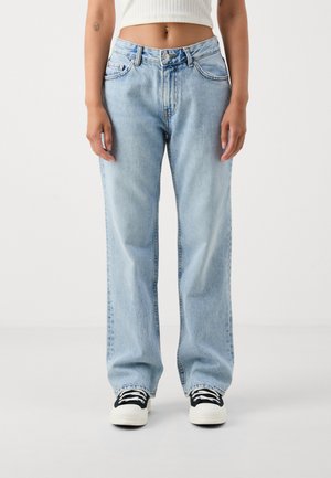 Jean en denim bleu clair à jambe large avec taille haute, présentant des poches classiques et des coutures, associé à des baskets noires et blanches.