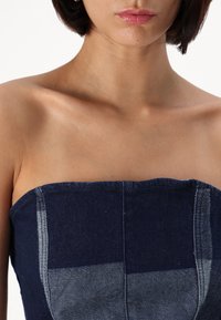 Top din denim fără bretele, cu țesătură albastră închisă și panouri contrastante de un albastru deschis, decolteu structurat și detalii de cusătură vizibile.