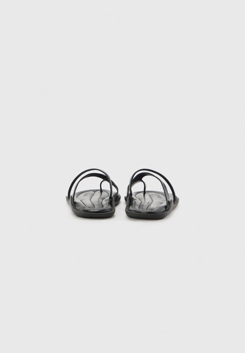 Chanclas negras con una suela plana y suave, que presentan múltiples tiras delgadas que crean un diseño minimalista. Plantilla texturizada con un patrón ondulado.