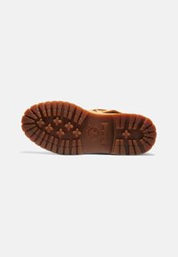 Semelle en caoutchouc marron présentant des crampons profonds et un logo de marque, avec un design texturé pour une meilleure adhérence et durabilité.