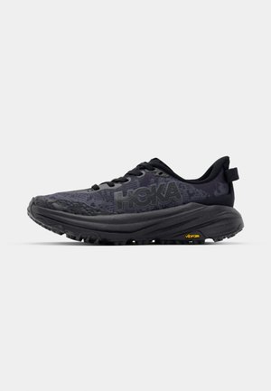 Black running shoe featuring a textured upper, rounded toe, and thick sole with a Vibram accent, designed for stability and grip.