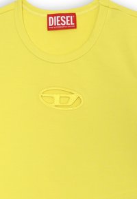 T-shirt di cotone gialla con collo rotondo. Presenta un logo ovale ricamato al centro, accentuato da cuciture tonali.