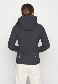 Veste à capuche noire avec une texture lisse, mettant en avant des accentuations blanches sur les zips et des poches latérales, conçue pour une silhouette ajustée.