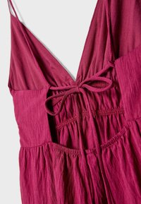 Robe bordeaux avec un décolleté en V profond et un lien ajustable à la taille. Présente un tissu texturé et fluide avec des détails froncés.
