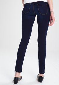 Smala jeans i mörkblå denim med en slät textur. Har två bakfickor och kontrasterande sömmar. Bärs med svarta klackskor.