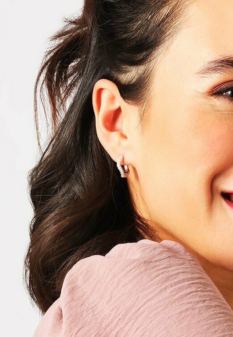 Orecchini a cerchio in argento con design ritorto, caratterizzati da piccoli accenti scintillanti. Il modello ha capelli scuri acconciati in onde morbide.