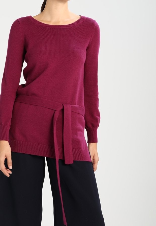 Femme portant un pull rose foncé à manches longues avec une ceinture nouée à la taille et un pantalon noir à jambes larges.