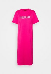 Jasnoróżowa midi sukienka T-shirt z krótkimi rękawami i białym napisem "HUGO" na piersi na jednolitym białym tle.