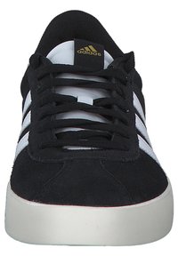 Sneaker in suede nero con design a tre strisce bianche, punta rotonda e suola in gomma bianca. Presenta il logo dorato sulla linguetta e lacci neri.