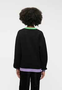 Sweater preto oversized com colarinho verde e bainha em roxo. Apresenta ombros caídos e textura suave, visto de trás.