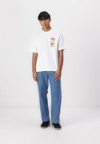 White cotton t-shirt with graphic print featuring pink and green elements, paired with light blue straight-leg jeans and black sneakers.