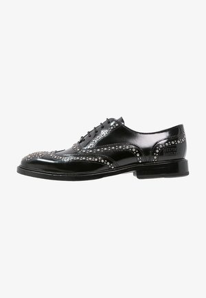 Zwarte gepolijste leren brogueschoen met zilveren studs, veters aan de voorkant, lage hak en gebrande hielkap.