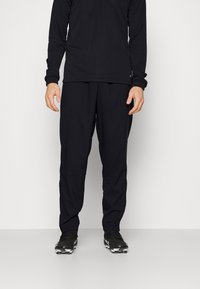 Svart atletisk outfit bestående av en långärmad topp och löst sittande byxor. Materialet verkar mjukt, slätt och flexibelt.