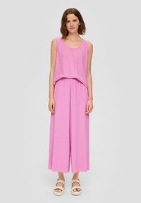 Roze mouwloze top en wijde broek van gestructureerde stof, met een losse pasvorm. Gecombineerd met lichte, strapless schoenen.