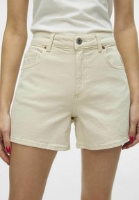 Bermudas de mezclilla beige con diseño ajustado, que cuentan con cierre de botón, bolsillos frontales y costuras visibles. Textura suave y largo corto.