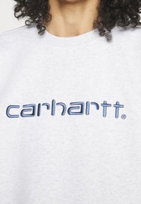Felpa grigia con collo a giro. Presenta il logo "carhartt" ricamato in blu sul petto. Tessuto morbido con una leggera trama.