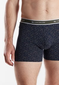 Dark blue boxer shorts with a geometric pattern in green, pink, and white. Features a branded elastic waistband and a snug fit.