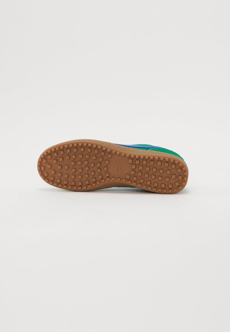 Suola di sneaker caratterizzata da una superficie in gomma marrone texturizzata con motivi di presa quadrati. Il bordo è leggermente rialzato e delineano la forma della scarpa.