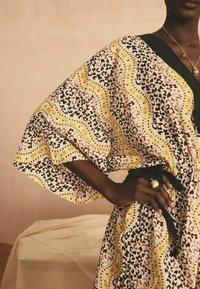 Kimono s uzorkom s mješavinom leopardskog uzorka i valovitih žutih akcenta. Izrađen od lagane tkanine s širokim rukavima i crnim remenom oko struka.