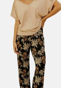 T-shirt rose clair à col en V ample avec des accents en dentelle, associé à un pantalon noir avec de grands motifs floraux dans des tons crème et rouille.