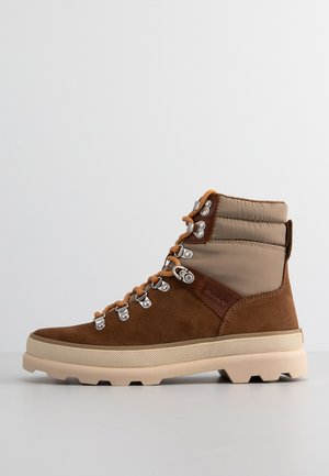Braune Wildleder-Wanderschuhe mit beigefarbenem gepolstertem Kragen, orangefarbigen Schnürsenkeln, Metallösen und einer strukturierten beigefarbenen Gummisohle für besseren Halt.