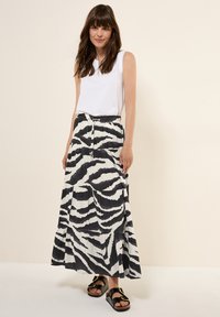Maxi gonna con stampa zebra in bianco e nero, caratterizzata da un design fluido, texture plissettata e vita elastica, abbinata a una maglietta senza maniche bianca e sandali neri.
