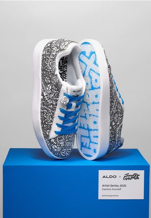 White sneakers with black abstract patterns, blue laces, and a textured blue sole. Features a heart charm. Supported on a blue pedestal.