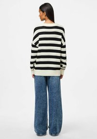 Maglione oversize a righe in nero e crema con polsini a coste, abbinato a jeans in denim blu sbiadito a gamba larga.