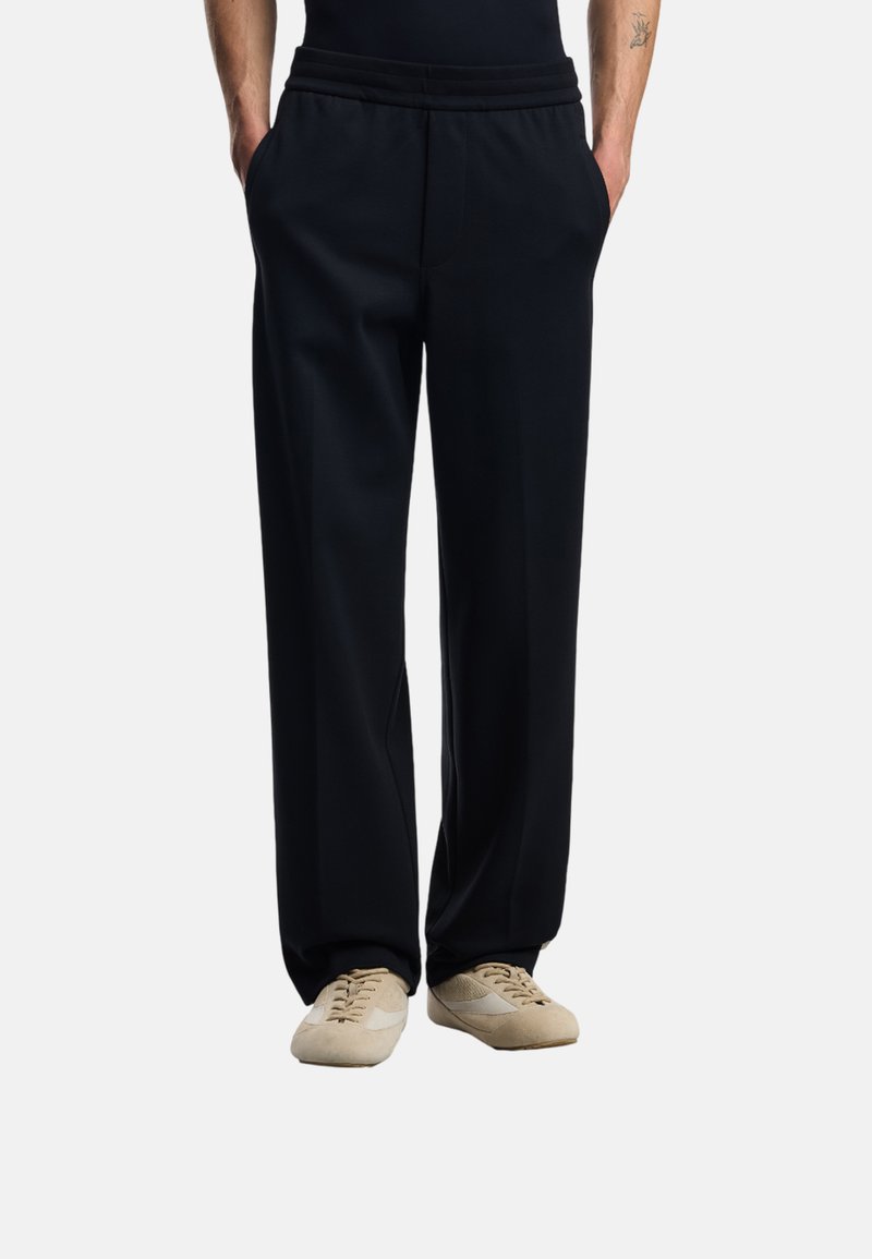 Svarta mjukisbyxor med en avslappnad passform, med en bred midja och sidofickor. Mjuk tyg med slät struktur, ihop med ljusbeiga skor.