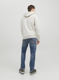 Felpa grigia chiara con cappuccio ampio, abbinata a jeans blu con vestibilità dritta. Le scarpe sono grigie con accenti neri. Design semplice.