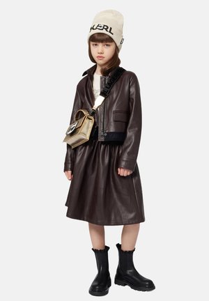 Veste cropped en cuir marron avec logo embossé, jupe assortie, bottes en caoutchouc noires à la cheville, et un bonnet en maille beige avec détail de logo.