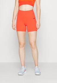 Shorts de sport rouges avec une taille haute, en matière extensible. Présentent un logo sur le côté gauche. Portés avec des baskets bleu clair.