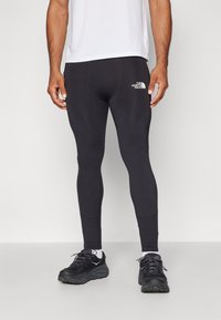 Svarta träningsleggings med en figurnära design, tillverkade av ett stretchigt material, med en vit logotyp på låret och sömdetaljer.