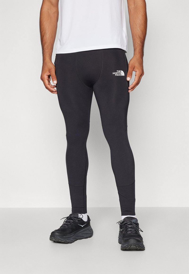 Svarta träningsleggings med en figurnära design, tillverkade av ett stretchigt material, med en vit logotyp på låret och sömdetaljer.