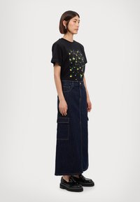 Zwarte t-shirt met een kleurrijke grafische print, gecombineerd met een lange spijkerrok met opgestikte zakken, en zwarte platform schoenen.
